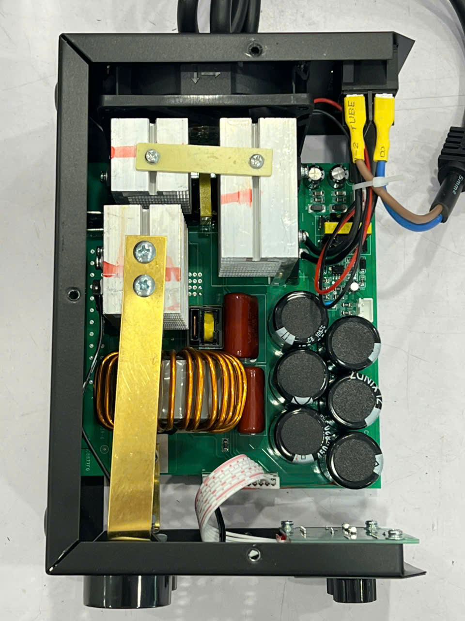 Internal view of a power supply board with large cooling fins, a copper coil, multiple capacitors, and assorted wiring.
